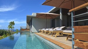 A modern infinity pool with wooden loungers and umbrellas, overlooking a scenic landscape.