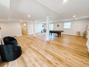 Une pièce spacieuse avec une table de billard, un plancher en bois et un fauteuil en forme de sac en tissu noir.
