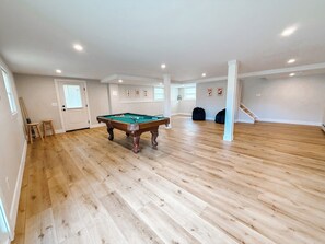 Une pièce spacieuse avec une table de billard, un plancher en bois et un escalier.