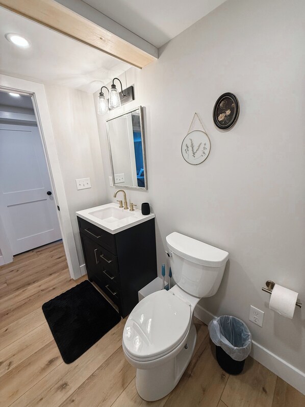 Une salle de bain moderne avec des toilettes blanches, un meuble-lavabo noir et un miroir au-dessus du lavabo.