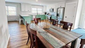 Une cuisine spacieuse avec des meubles blancs, une grande table à manger en bois et un réfrigérateur.