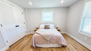 Une chambre à coucher avec un lit, deux tables de chevet, une fenêtre avec des stores et une porte.