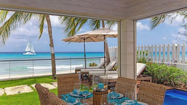 Un espacio de comedor al aire libre cubierto con vistas al océano y un velero.
