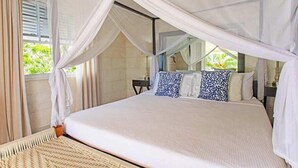 Una cama con dosel, ropa de cama blanca y almohadas estampadas.
