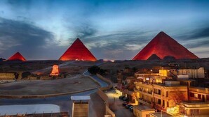 Three illuminated pyramids at dusk with a town in the foreground. - Pyramids Hotel (Giza)