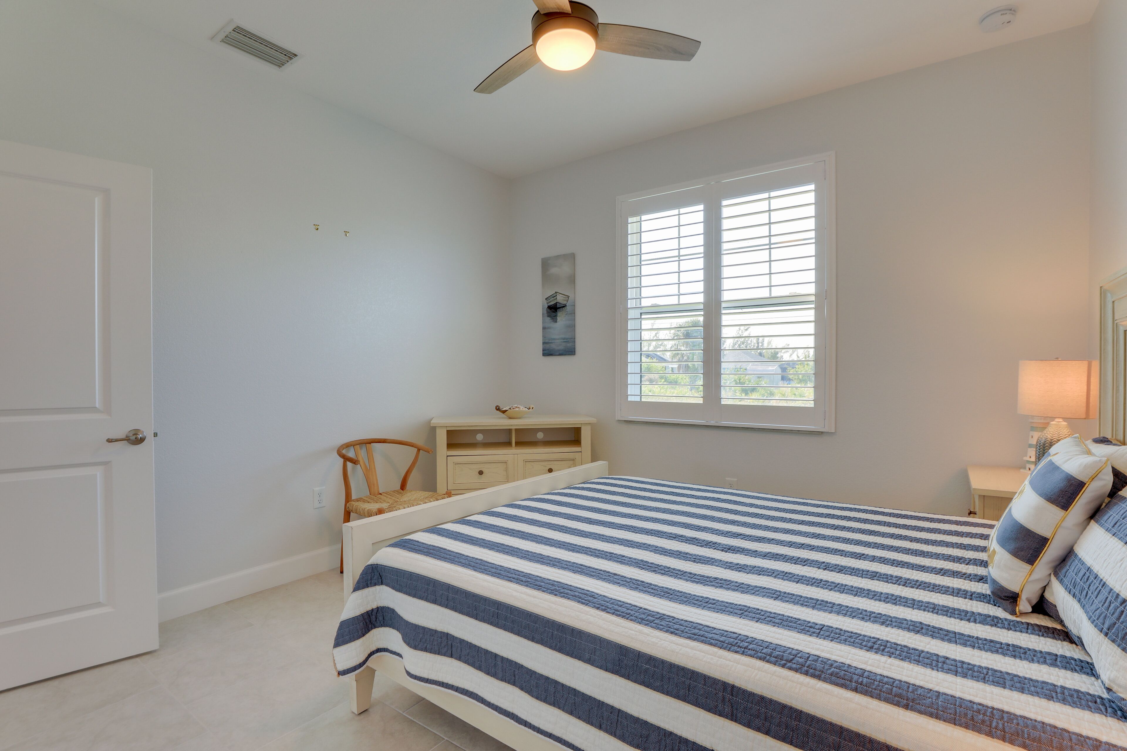 Un dormitorio con cama, escritorio, silla, ventana y ventilador de techo.