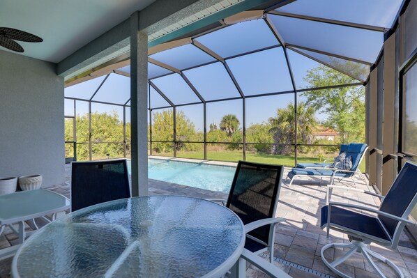 A covered outdoor area with a glass table and chairs, a pool, and a view of the surrounding landscape.