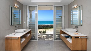 Une salle de bain moderne avec deux vasques, des meubles en bois et une vue sur la mer grâce à des portes vitrées.
