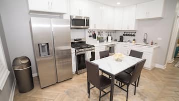 Una cocina moderna con electrodomésticos de acero inoxidable, armarios blancos y una zona de comedor con mesa de mármol.