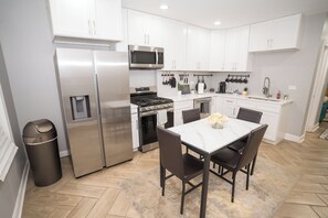 A modern kitchen with stainless steel appliances, white cabinetry, and a dining area with a marble table.