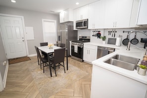 Una cocina moderna con gabinetes blancos, electrodomésticos de acero inoxidable y un suelo de madera en patrón de espiga.