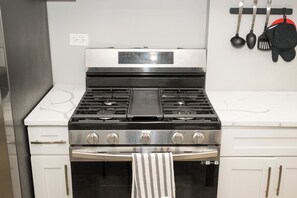 A kitchen with a stainless steel stove, a microwave, and a built-in oven. There is a white countertop and a hanging utensil rack with pots and pans. - Toca Bella ~ 7mins to Downtown
 (Chicago)