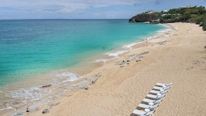 Une plage à l’eau turquoise et limpide, une rangée de chaises longues et une côte rocheuse.
