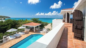 Un espace aménagé au bord de la piscine, avec vue sur l’océan, des sièges extérieurs et une terrasse couverte.
