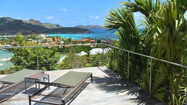 A balcony with a view of a coastal area, including a beach and mountains.