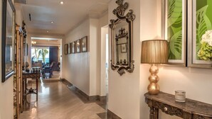A hallway with a polished floor, a decorative console table with a lamp, and framed mirrors on the walls.
