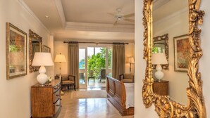 A hotel room with a large ornate mirror, a bed, a wooden dresser, and a view of the outdoors through large windows.