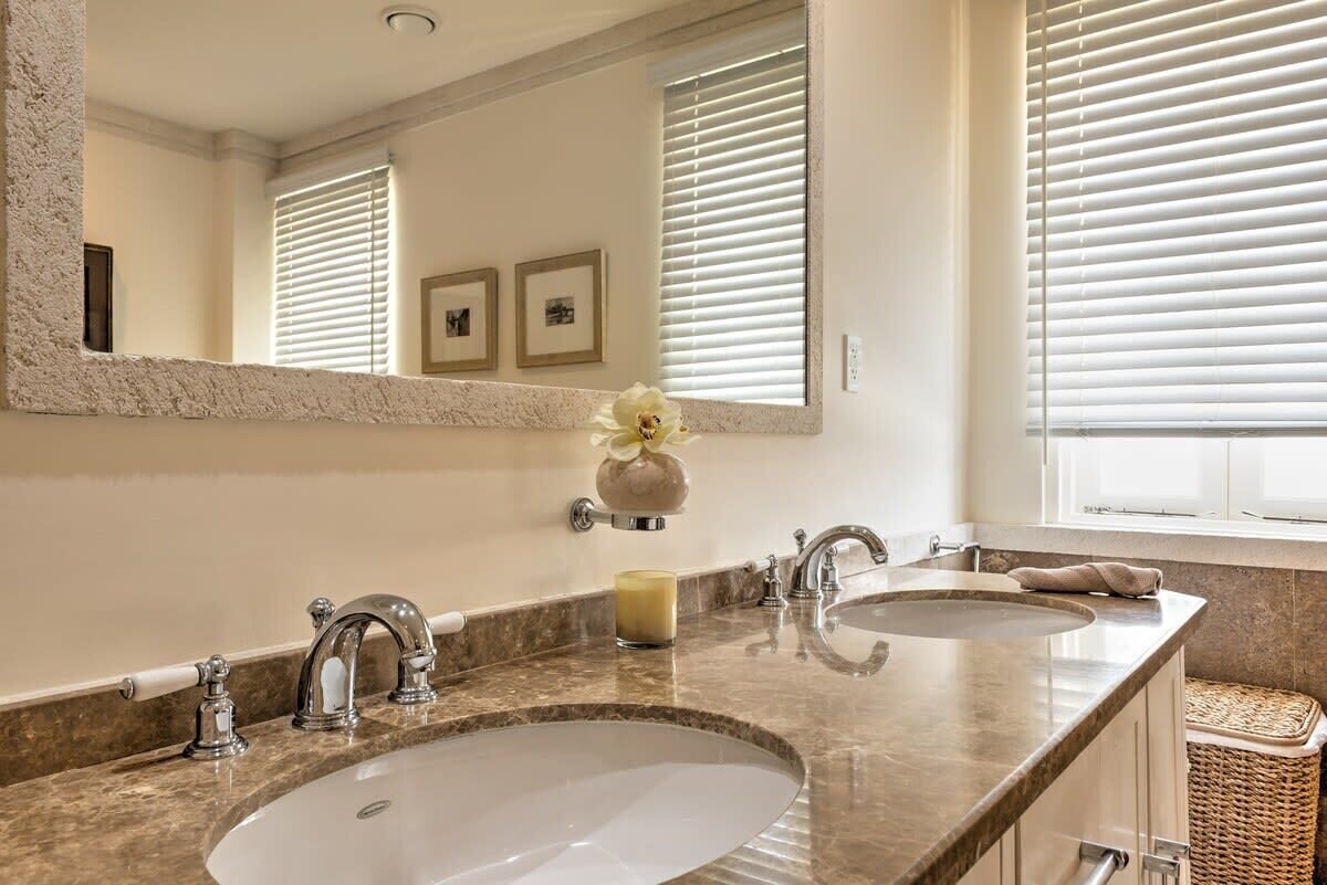 A bathroom with two sinks, a large mirror, and a window with blinds.