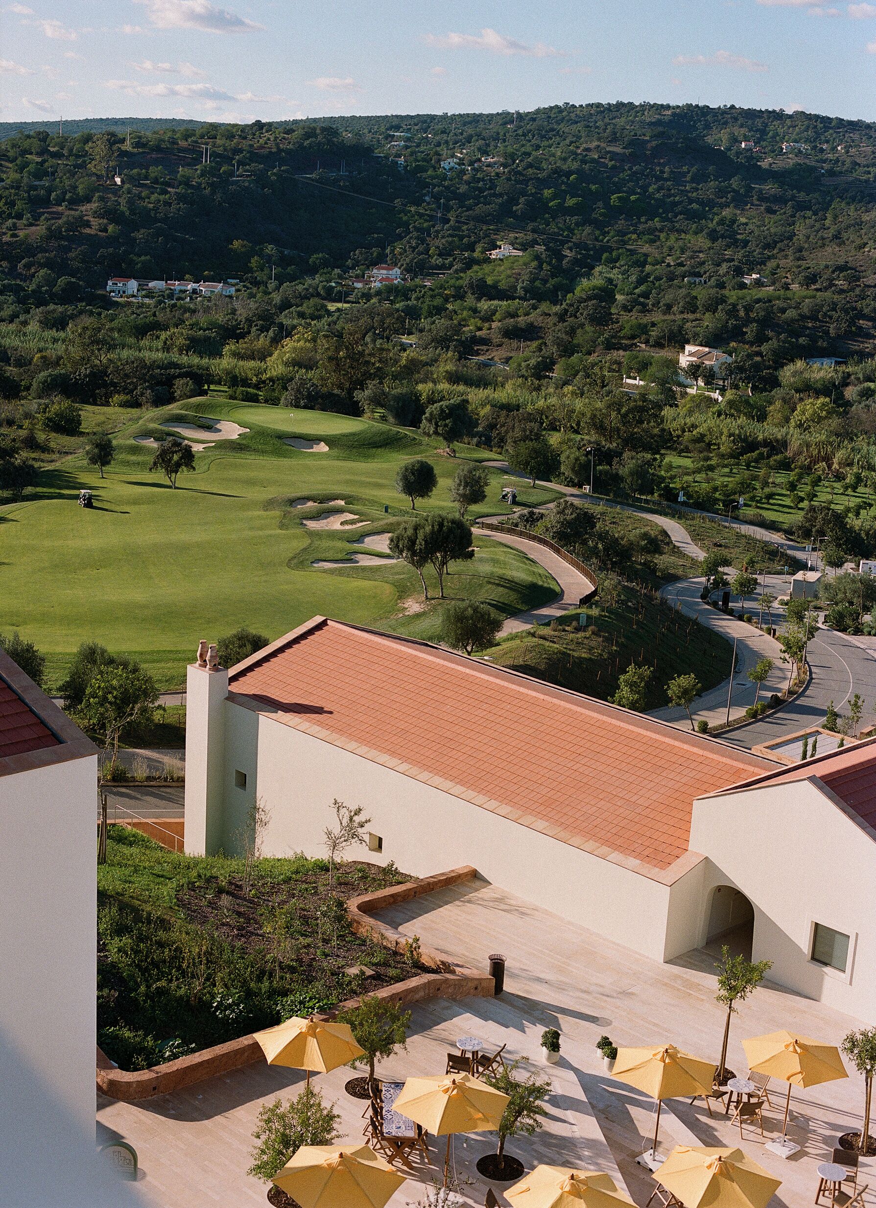 Campo de golf con vista a un edificio de techo de tejas y zona de estar al aire libre con sombrillas.