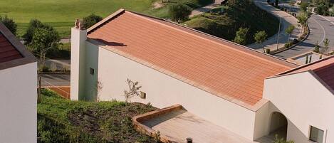 A golf course with a view of a building with a tiled roof and outdoor seating area with umbrellas.