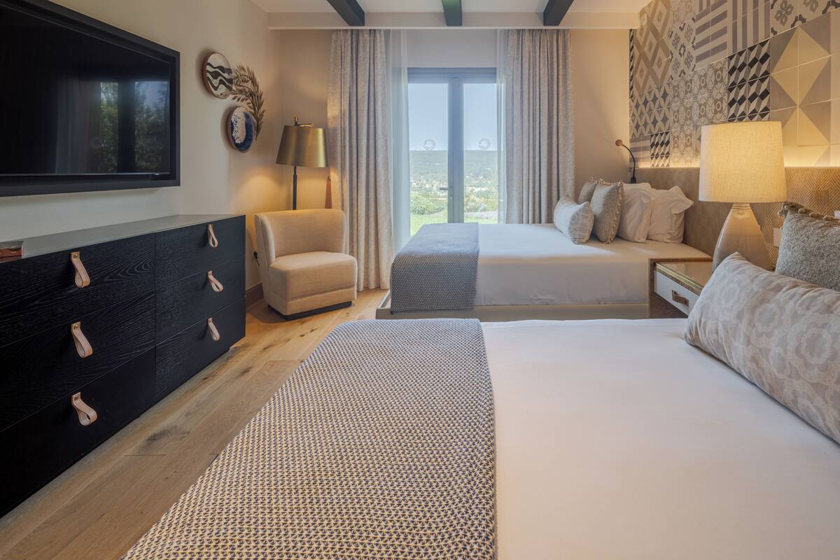 Une chambre d’hôtel moderne dotée d’un grand lit, d’un lit plus petit, d’un bureau, d’une télévision et offrant une vue sur l’extérieur.