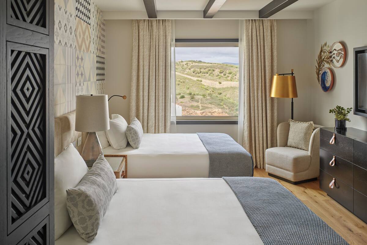 Une chambre d’hôtel avec deux lits, un canapé, une télévision et une grande fenêtre donnant sur un paysage désertique.