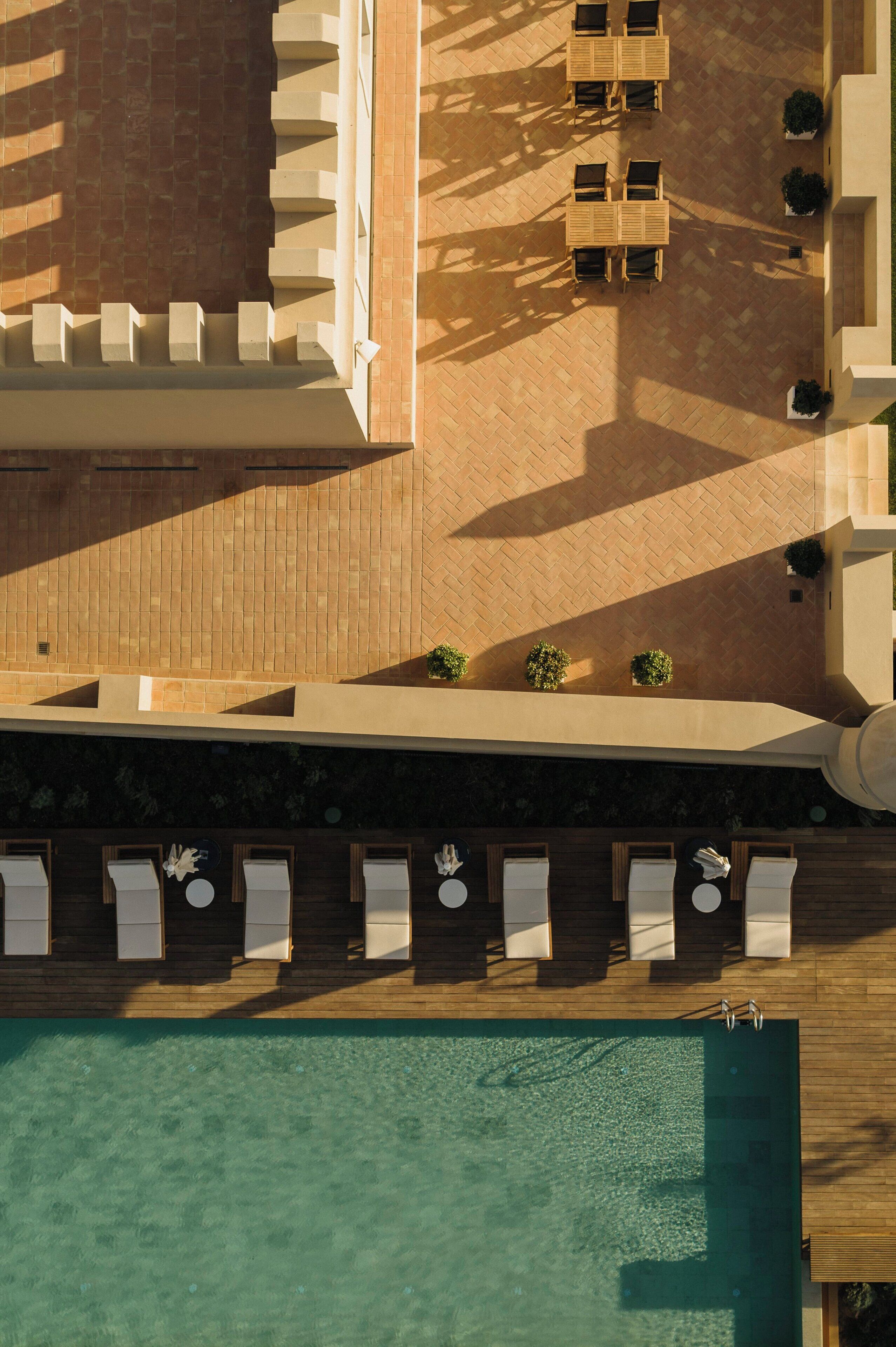 An aerial view of a hotel with a swimming pool, outdoor seating area, and a covered patio.
