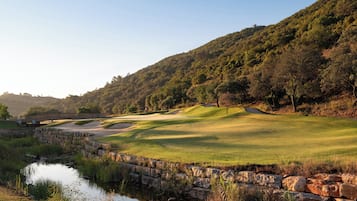 Stroll across the wooden bridge to a serene golf course with a well-maintained fairway, sand bunkers, and a tranquil water body.