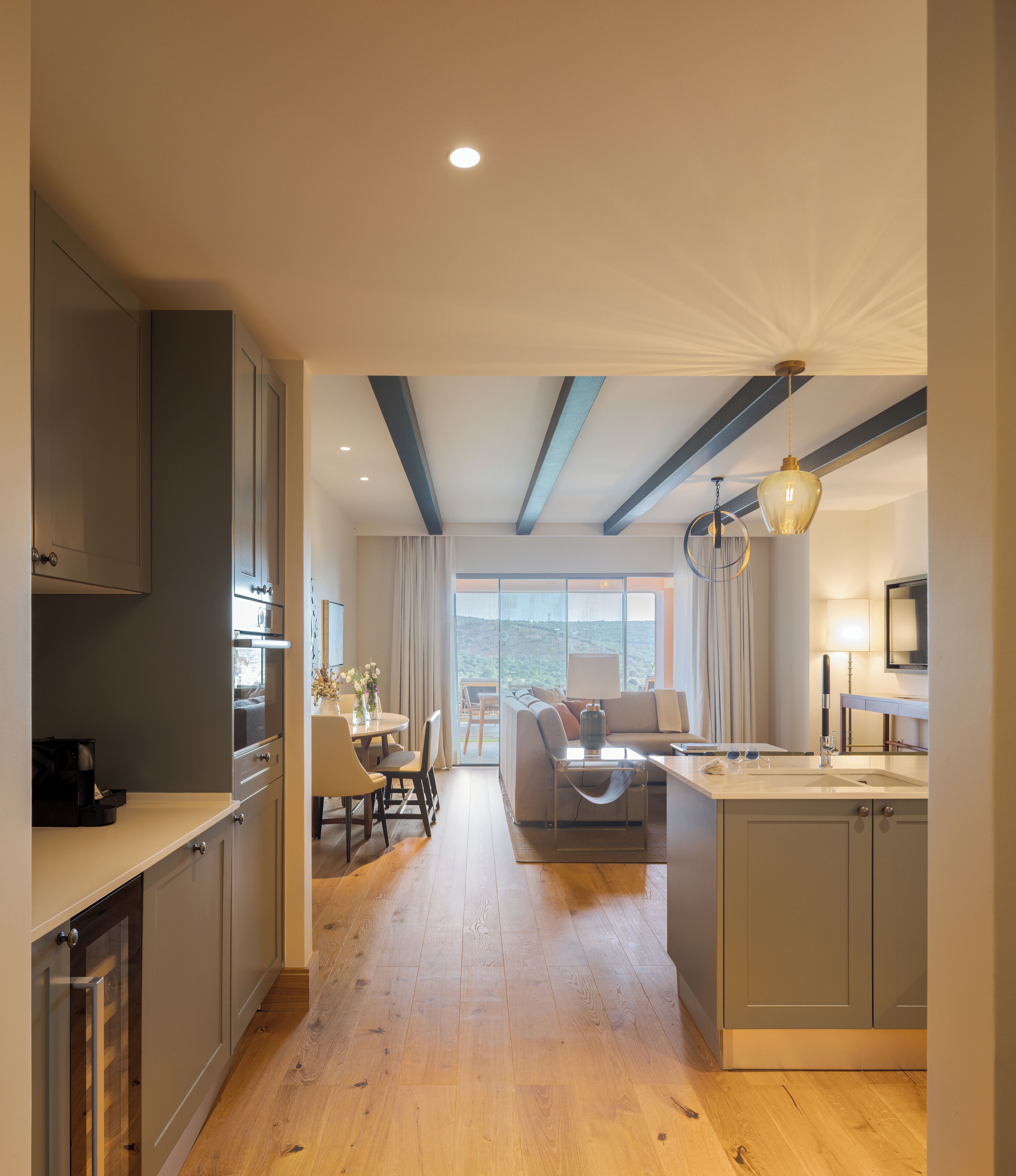 A modern kitchen with wooden flooring, a dining area with a table and chairs, and a view of the outdoors.