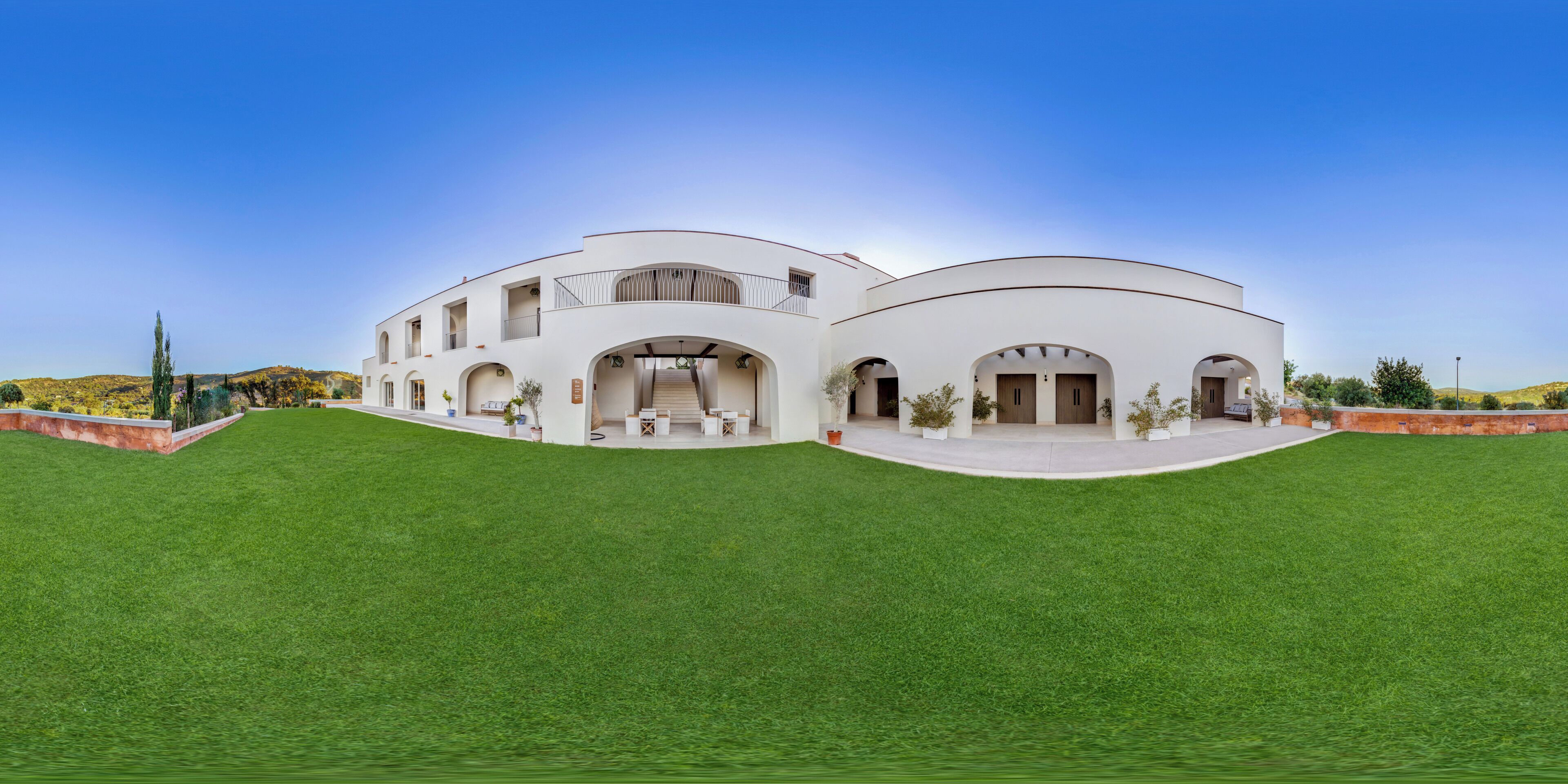 A modern white building with multiple arches and a flat roof, surrounded by a well-maintained lawn.