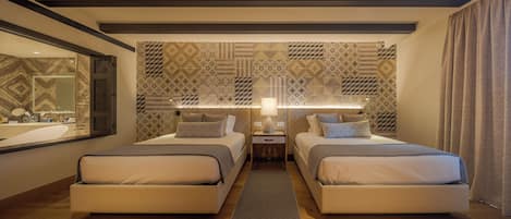 A hotel room with two beds, a large mirror, patterned wallpaper, and a nightstand with a lamp.