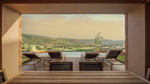 A deck with lounge chairs overlooking a pool and a scenic view of hills.