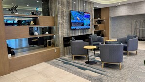 Un hall d’hôtel moderne comprenant un comptoir d’accueil, un espace salon et un grand écran de télévision diffusant les actualités.