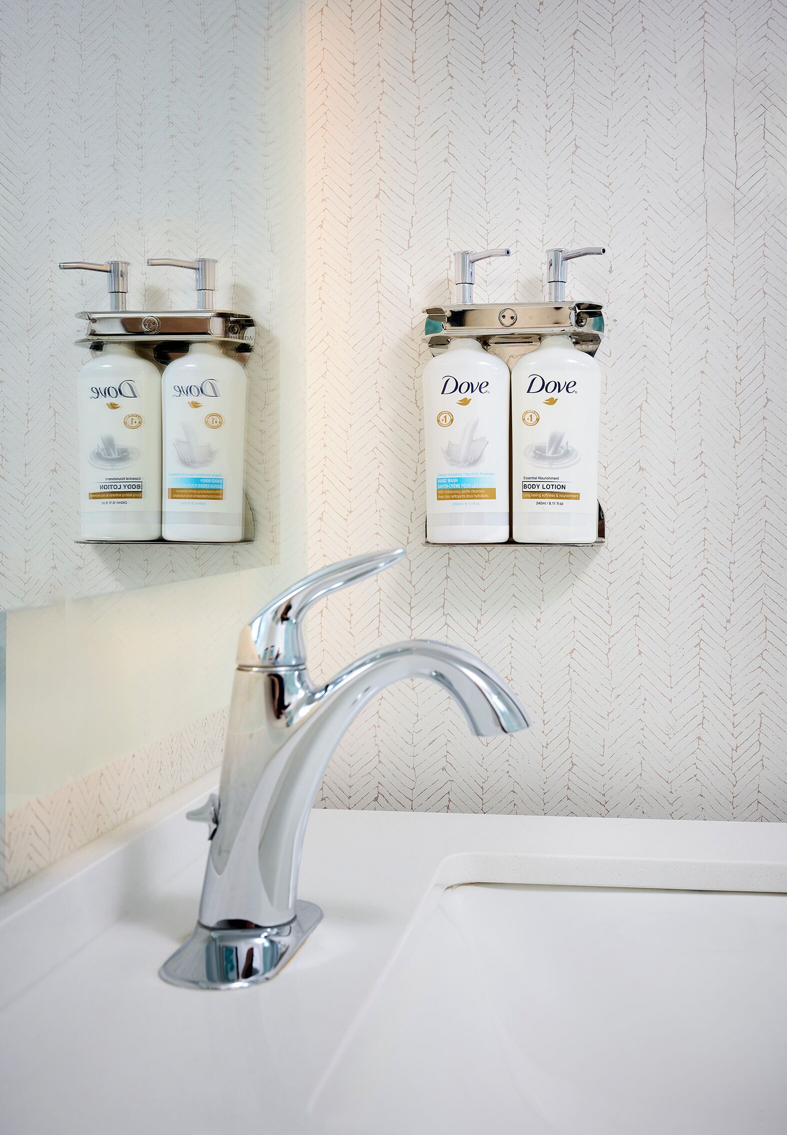 Un baño con un lavamanos moderno, grifo cromado y dispensadores de loción corporal Dove montados en la pared.