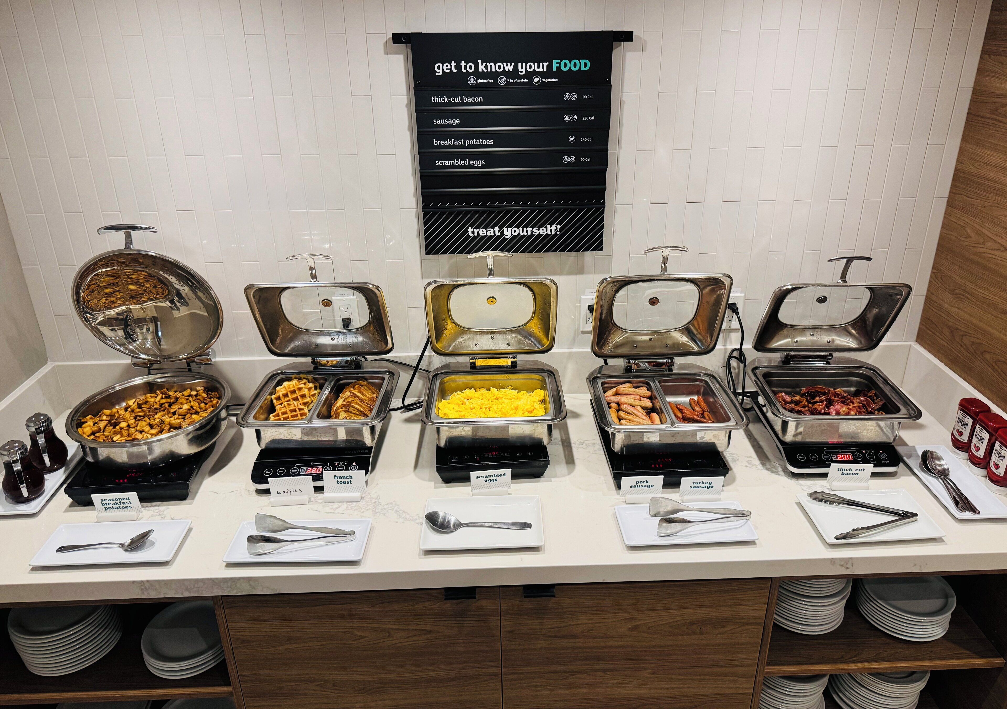 Ein Frühstücksbuffet mit verschiedenen Speisen, darunter Rührei, Wurst und Waffeln.