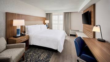 A hotel room with a bed, bedside tables with lamps, a desk with a chair, a TV, and a patterned rug.