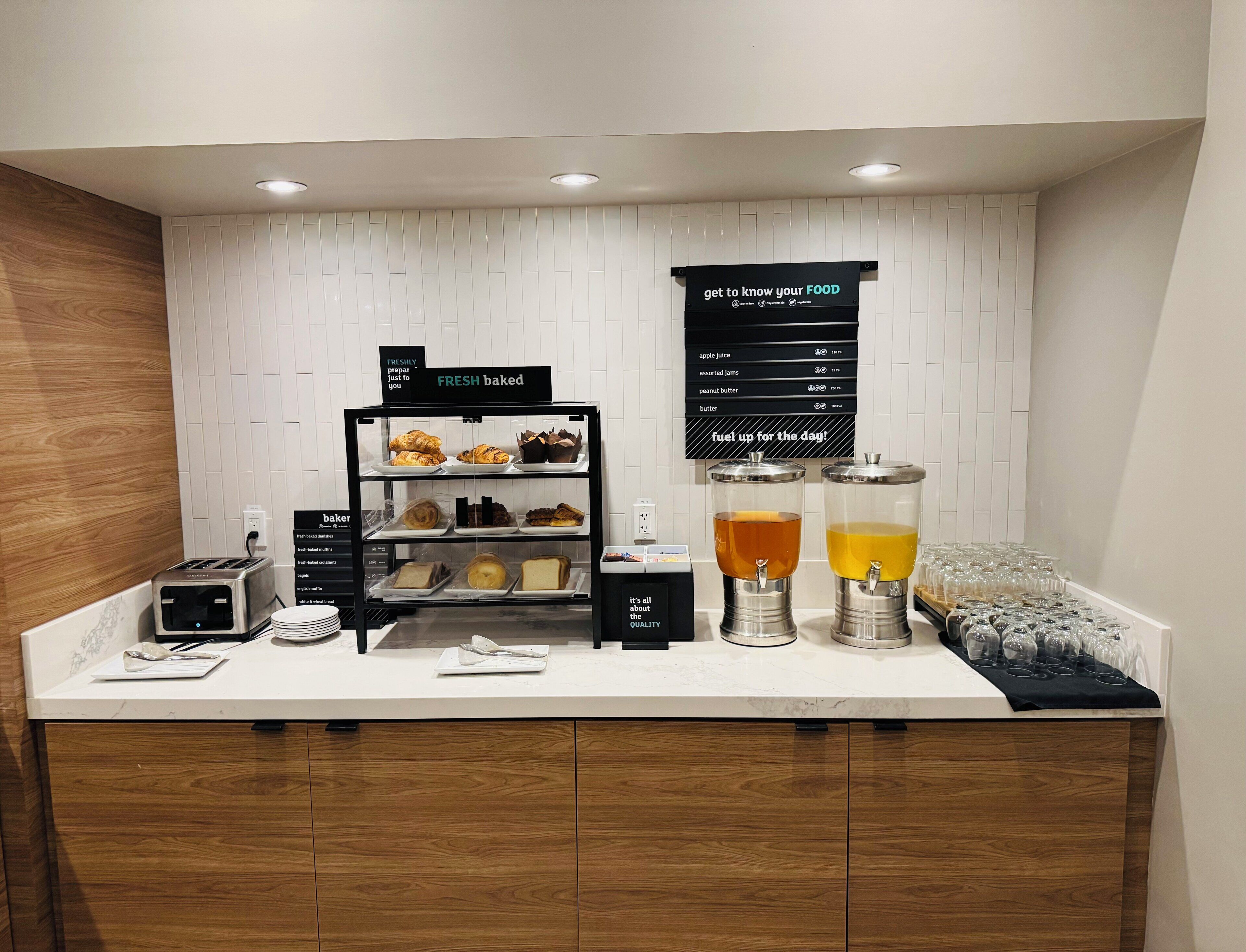 A breakfast bar with a selection of pastries and beverages, a toaster, and a sign indicating freshly baked goods.