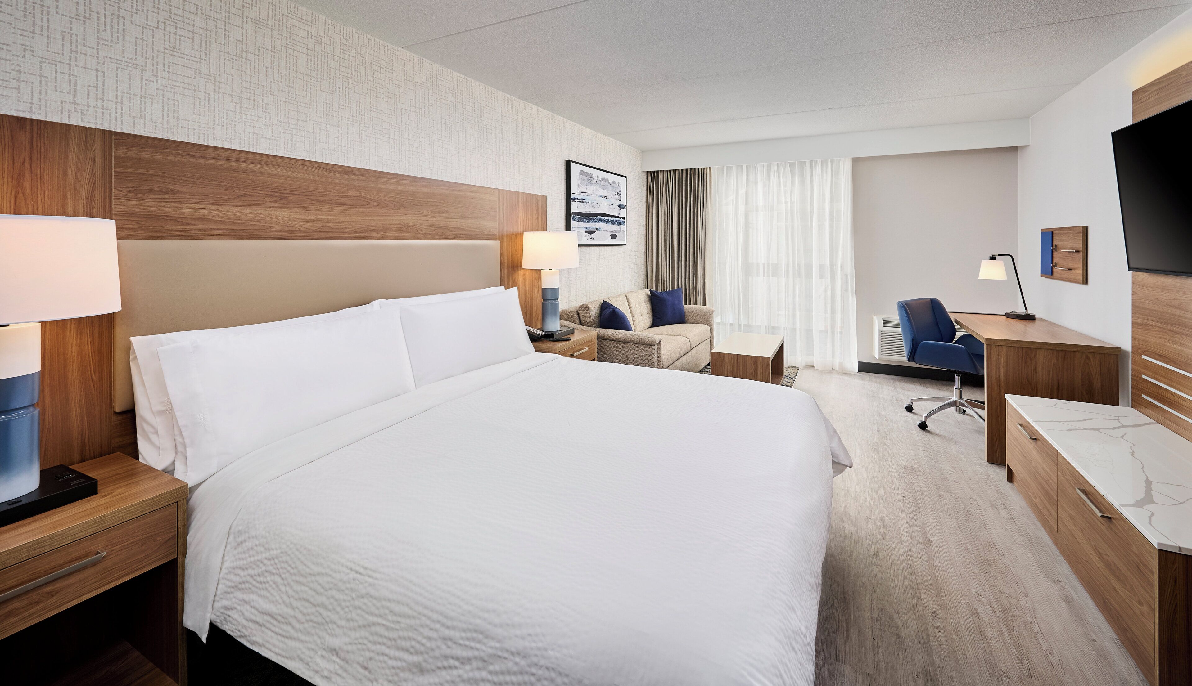 Ett hotellrum med en stor säng, ett skrivbord, en stol och en tv.