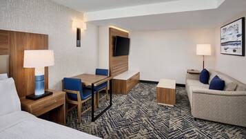 Habitación de hotel con cama, escritorio con silla, sofá, televisión y alfombra estampada.