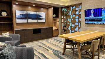 Una sala moderna con un mueble de entretenimiento de madera, un televisor de pantalla plana grande, un tapete estampado y una zona de comedor con mesa y sillas de madera.