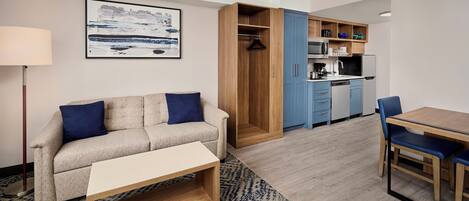 Habitación moderna con sofá, mesa de comedor, zona de cocina y una obra de arte colgada.