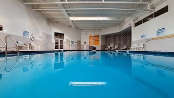 Une piscine intérieure à l’eau claire, dotée d’un plongeoir et bordée de chaises longues le long des murs.