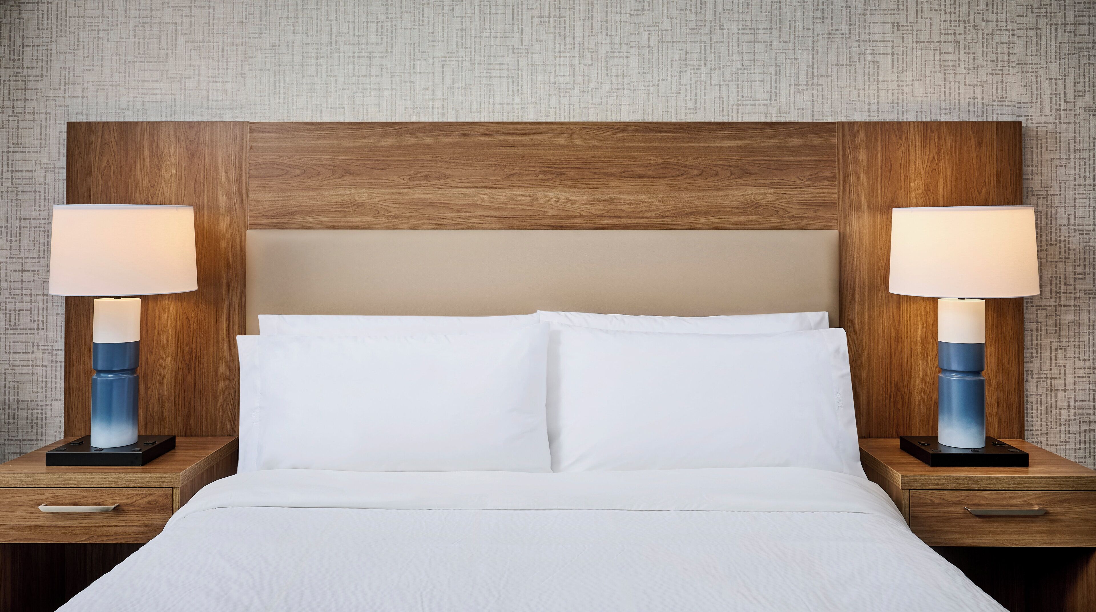 A hotel room with a wooden headboard, two bedside tables with lamps, and a bed with white linens.