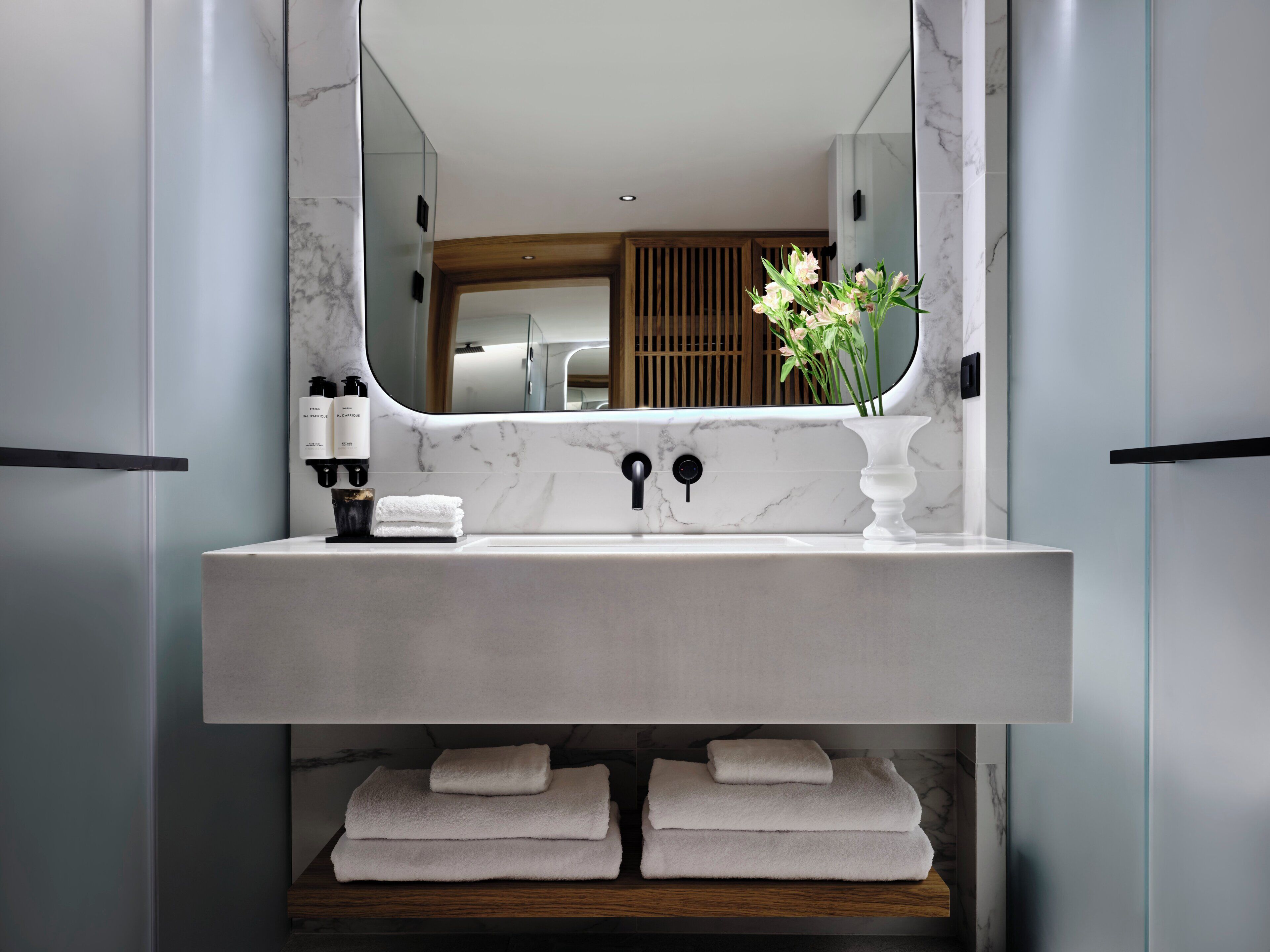Ein modernes Badezimmer mit Marmorwaschbecken, einem Spiegel und einer Vase mit Blumen.
