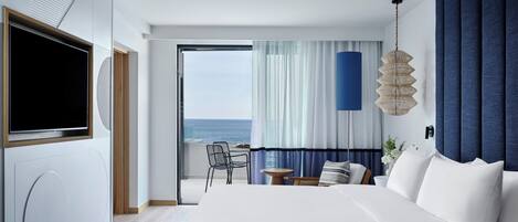 Une chambre d’hôtel moderne dotée d’un grand lit, d’une télévision, d’un balcon avec vue sur la mer et d’un coin repas.