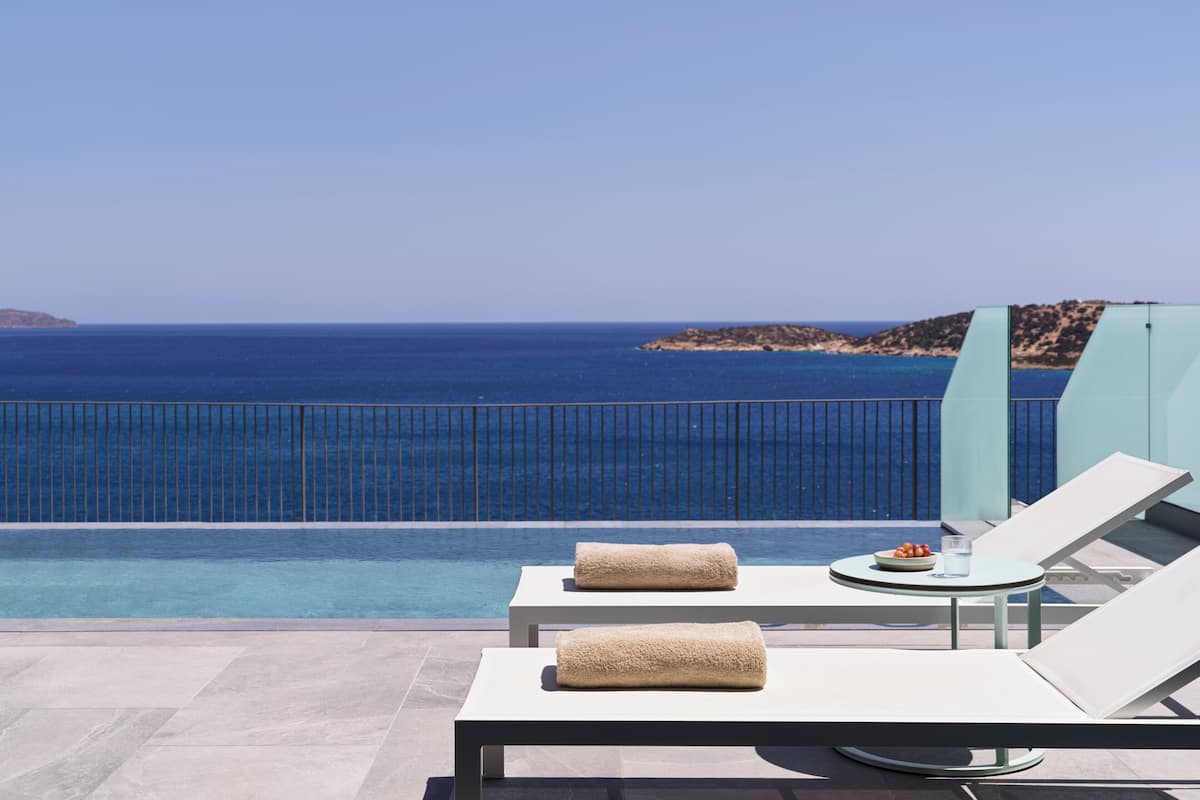 Ein Poolbereich mit Liegestühlen und Handtüchern mit Blick auf das klare, blaue Meer und das entfernte Umland.