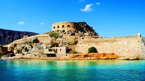 Une forteresse historique en pierre, dotée d’une tour ronde, située sur le flanc d’une colline rocheuse et offrant une vue imprenable sur une mer bleue et limpide.