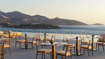 An outdoor dining area with tables and chairs, overlooking a body of water and hills.