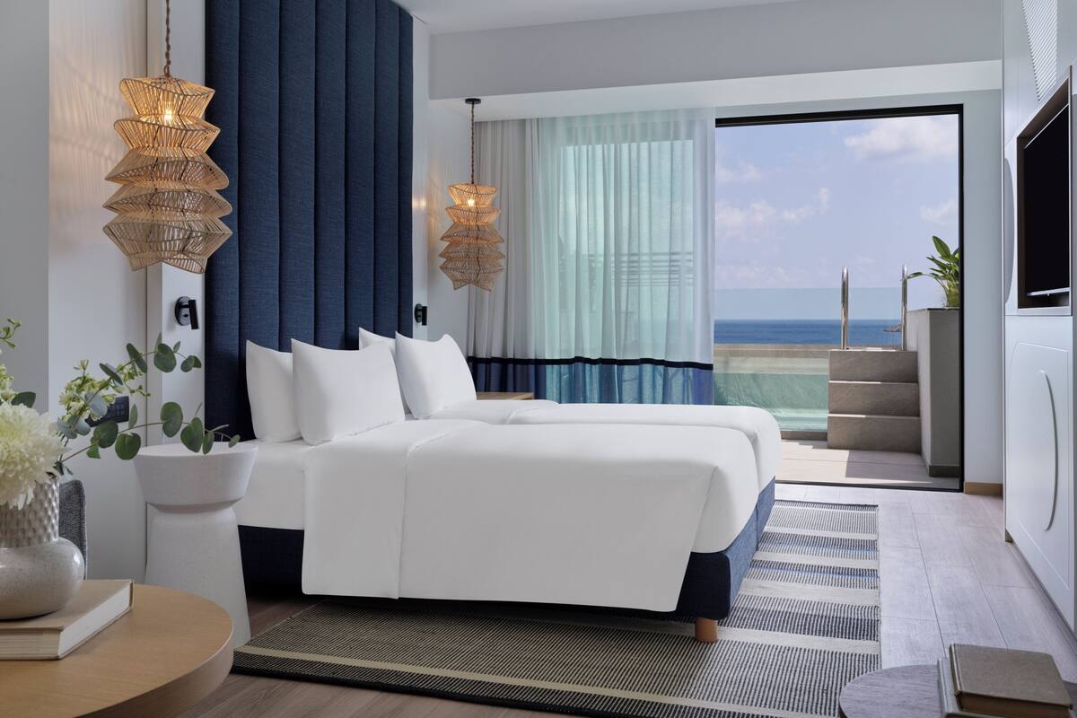 Ein modernes Hotelzimmer mit einem großen Bett, Meerblick und einem Balkon mit Pool.