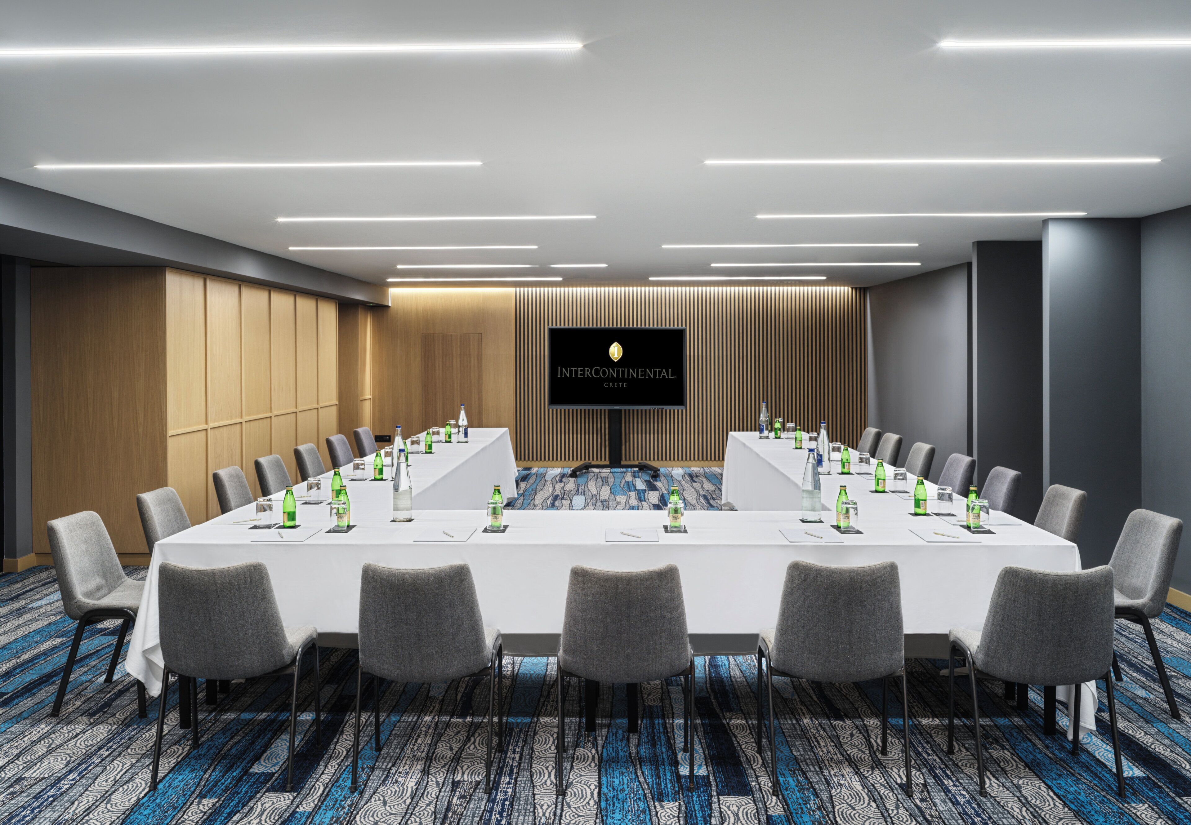 A conference room with a long table, chairs, and a large screen displaying "INTERCONTINENTAL CREST".